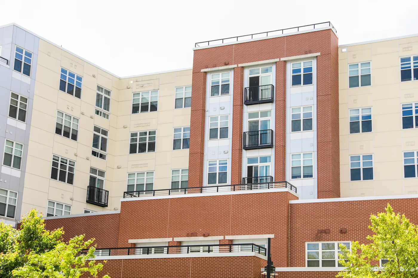 Multi-story university residential dormitory building with cream-colored walls, red brick sections, numerous windows, balconies, and trees in front.