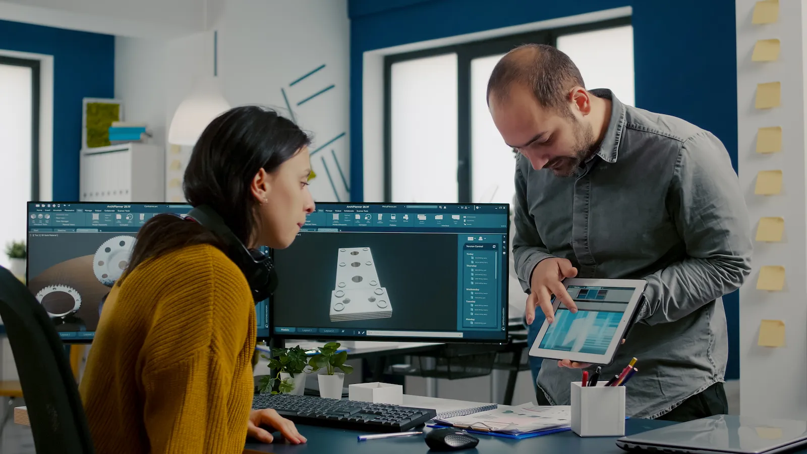 Two engineers reviewing a 3D building model on dual monitors at a desk in an office