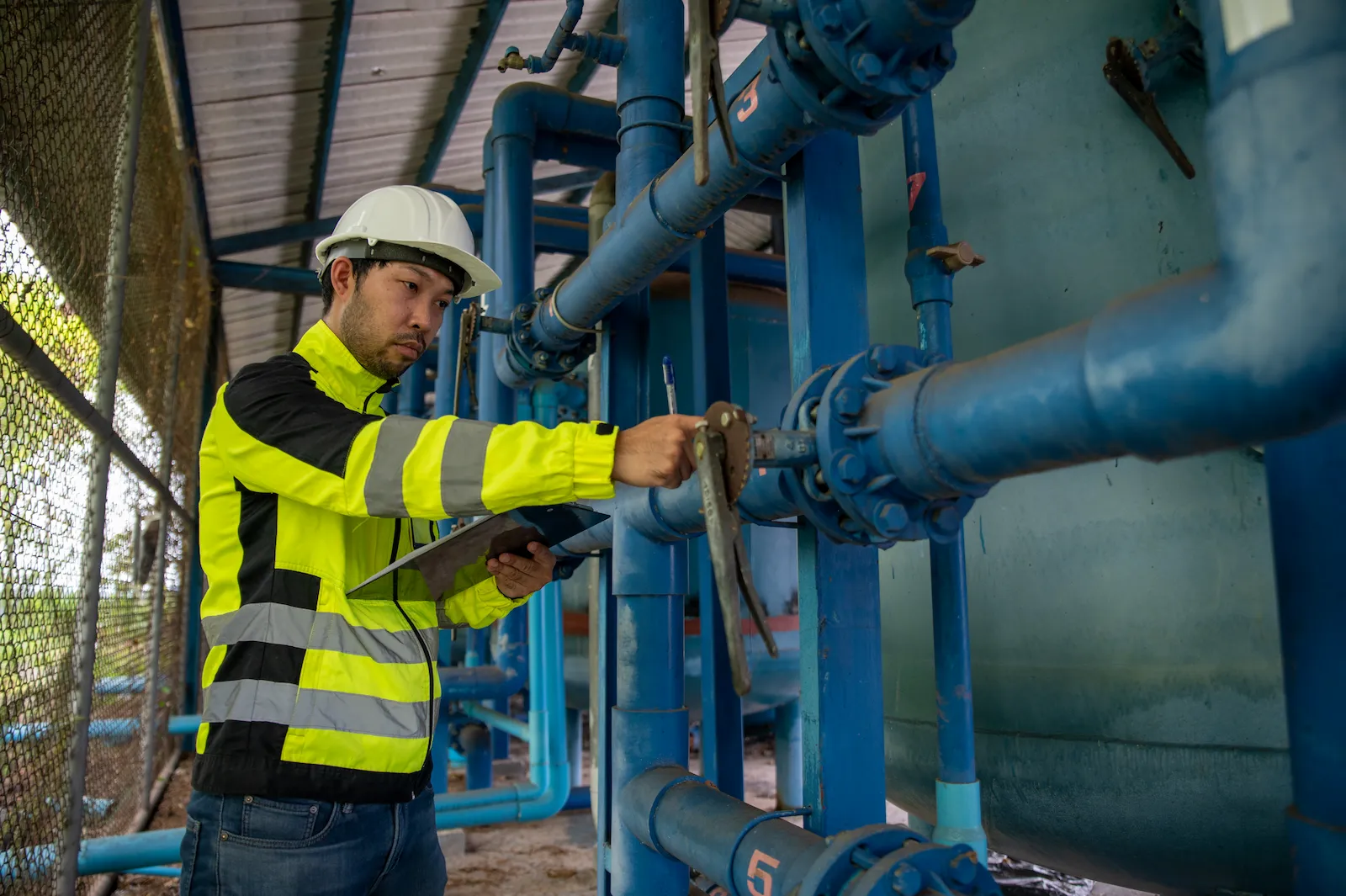A plant engineer in a safety helmet inspecting pipework and valves