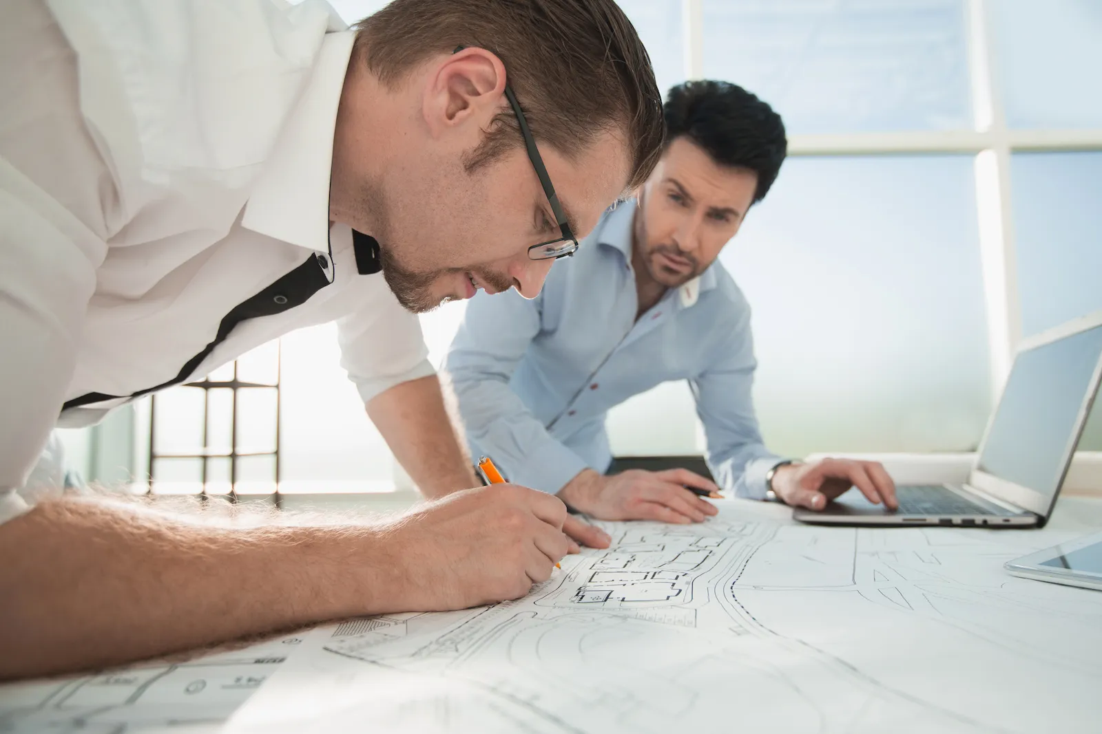 Two engineers reviewing a structural drawing together at a desk in a daylit office